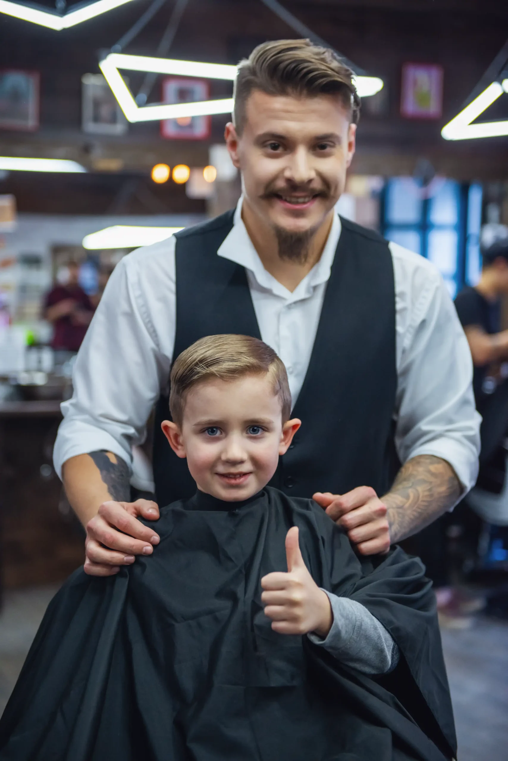 An elementary-aged boy giving a thumbs up after kids' haircut services with his barber.